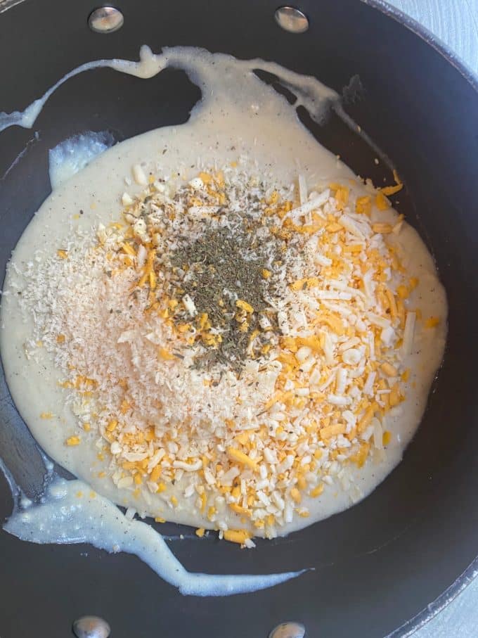 overhead shot of a nonstick skillet with a white roux inside, the roux is topped with a blend of shredded cheese