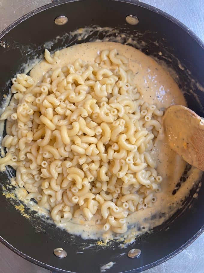 overehead shot of a nonstick skillet with a vegan cheese sauce being mixed with cooked elbow macaroni