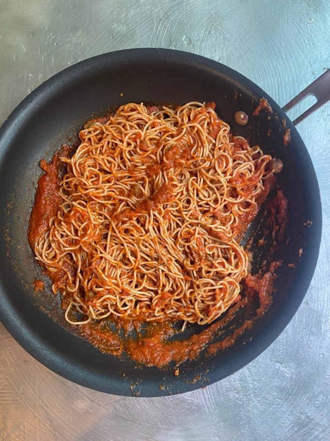 overhead shot of a skillet filled with cooked spaghetti tossed with a red sauce