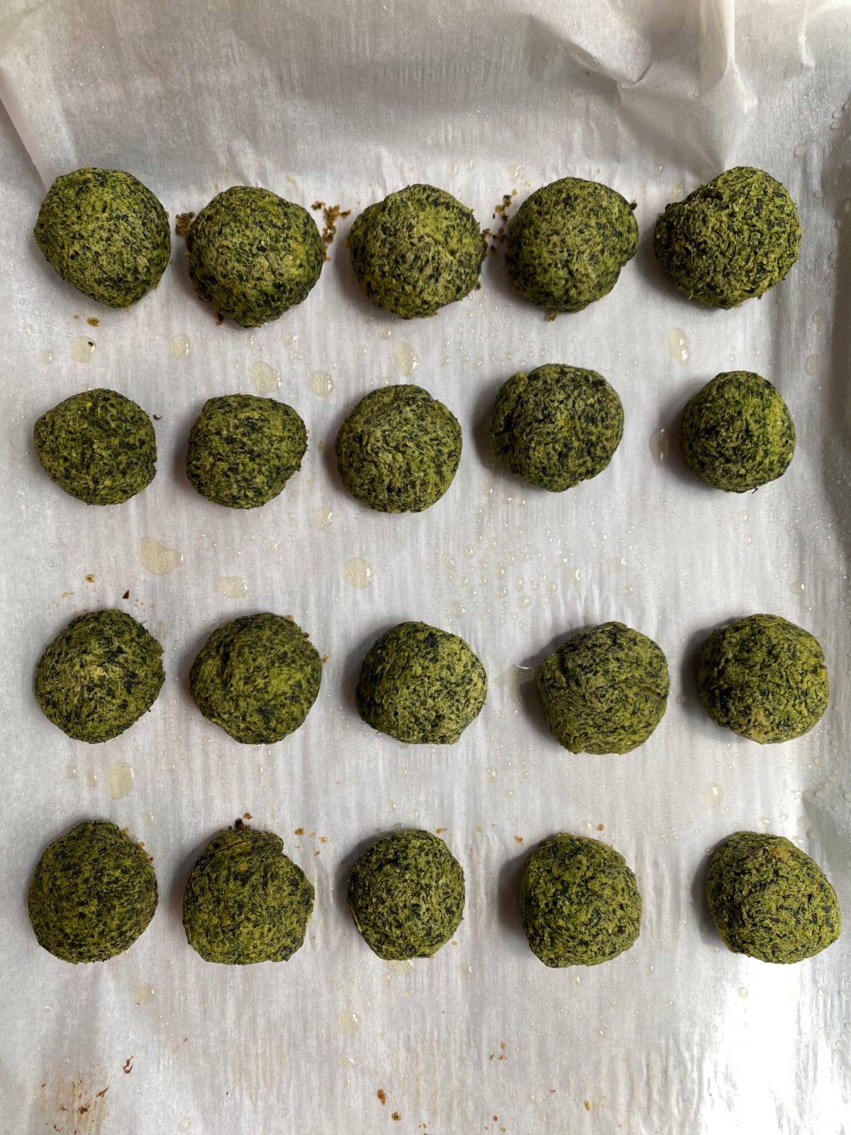 overhead shot of 20 spinach vegan meatballs on a parchment paper lined sheet tray 