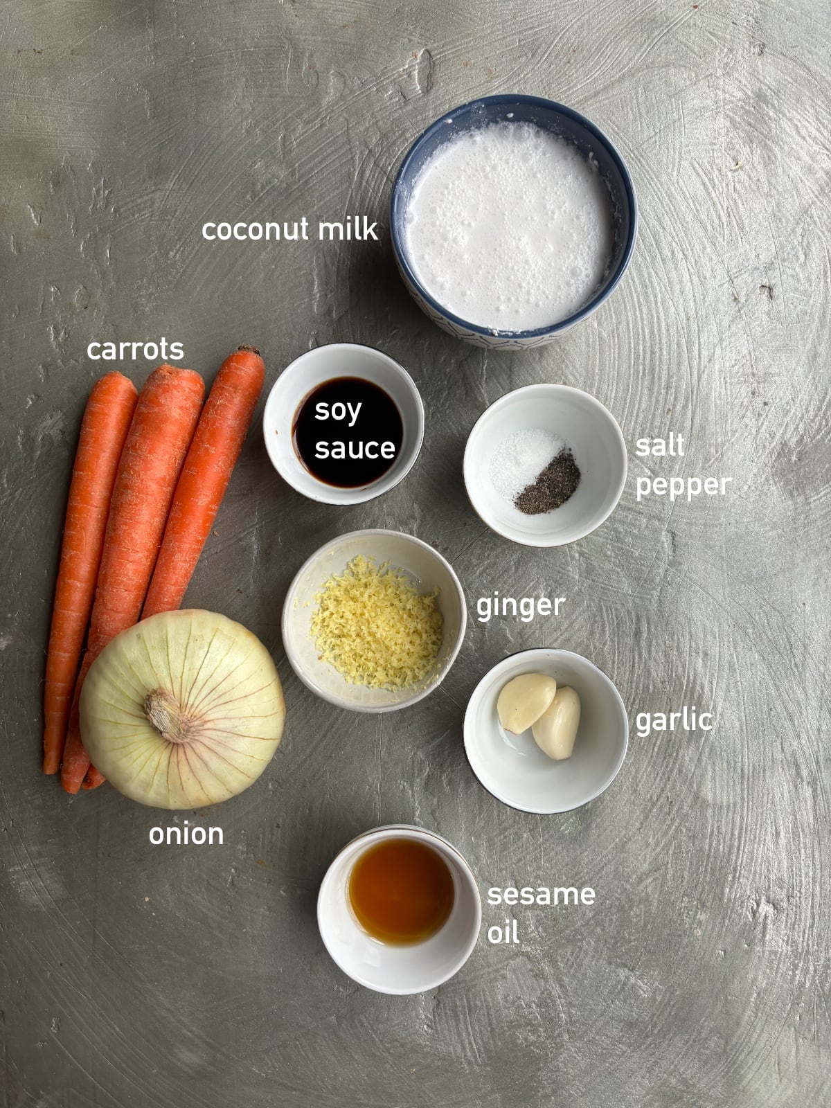 overhead shot of the ingredients needed to make Carrot Ginger Soup, each in small bowls and labeled with white font