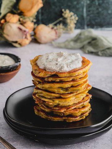 A close up image of a tall stack of Savory Chickpea and Scallion Pancakes topped with Labneh Caper Sauce.