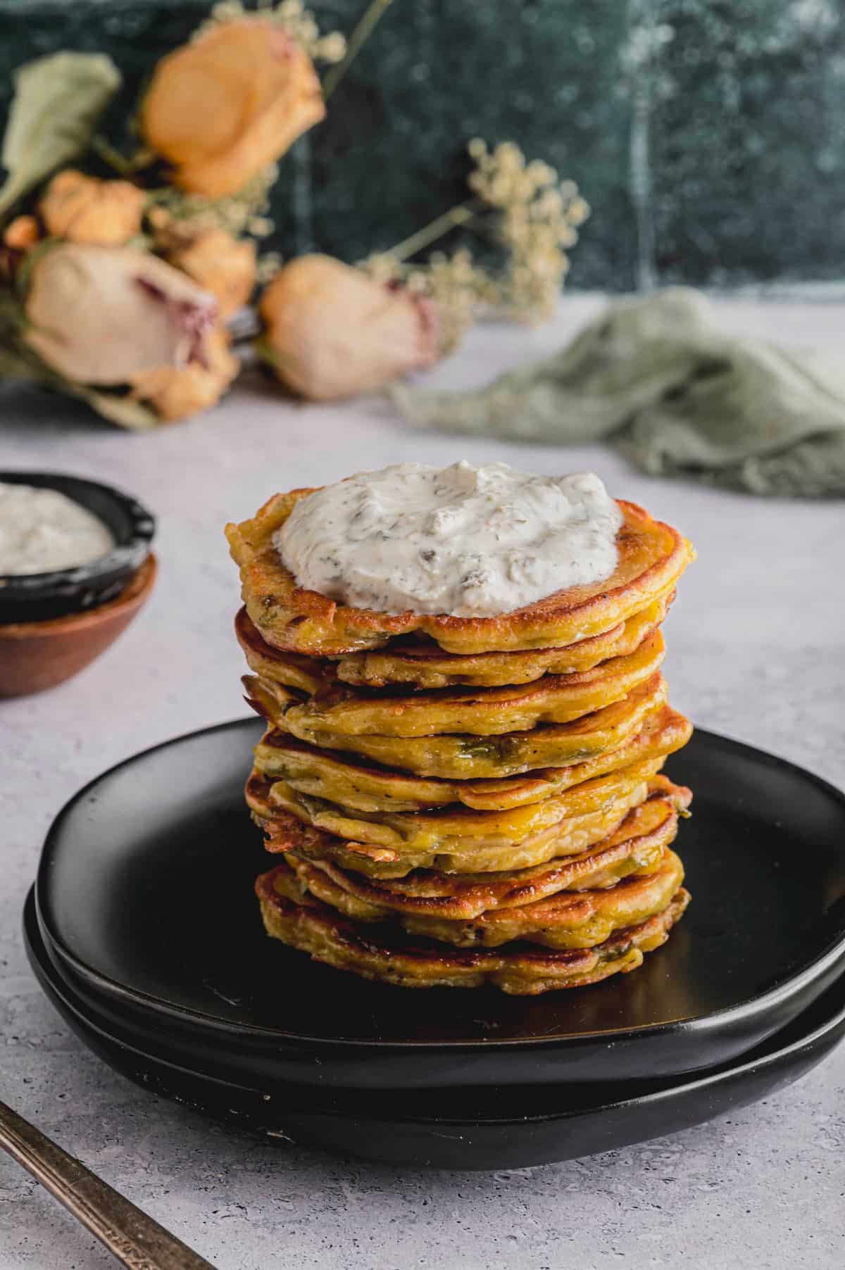 A close up image of a tall stack of Savory Chickpea and Scallion Pancakes topped with Labneh Caper Sauce. 