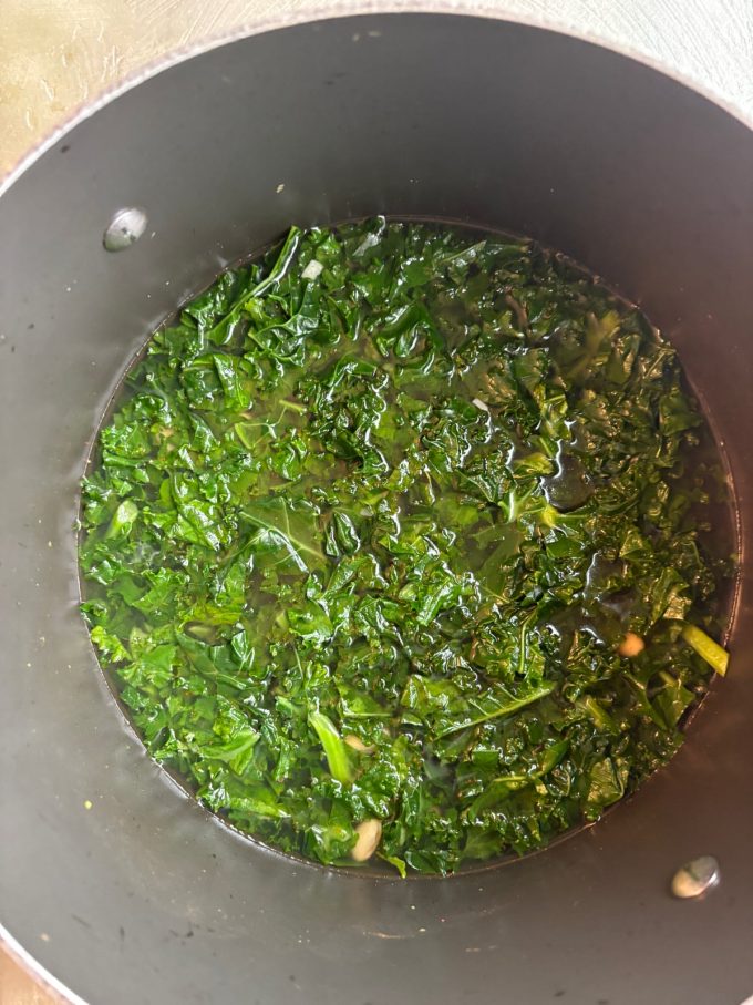 overhead shot of chopped kale covered with broth in a pot
