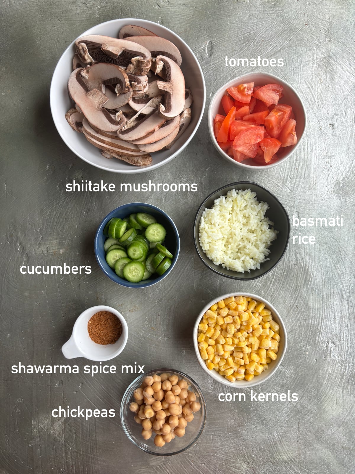 overhead shot of several small bowls containing the ingredients needed to make rice bowls with shawarma spiced mushrooms, each labeled with white text