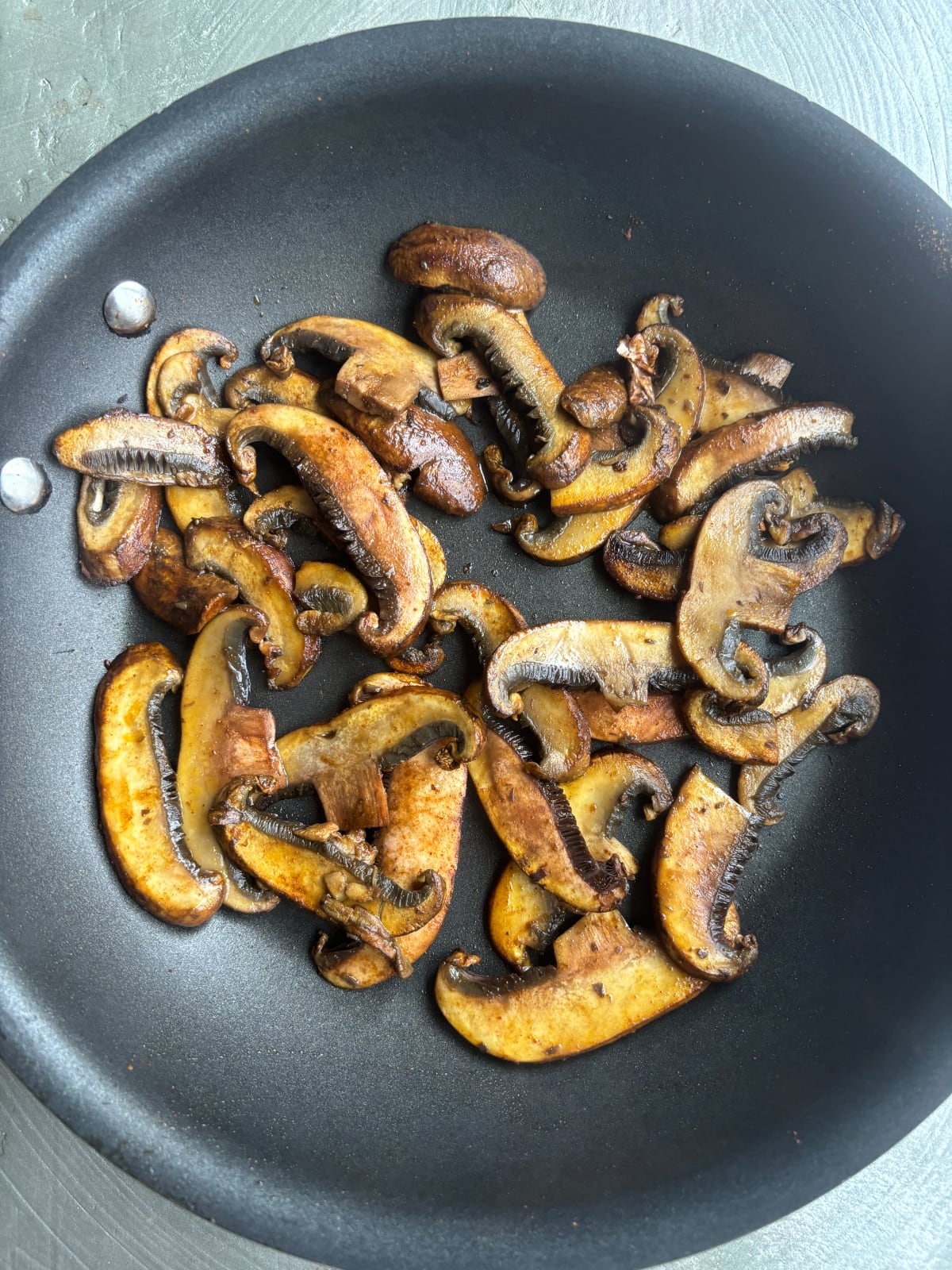 overhead shot of a skillet cooking sliced shiitake mushrooms tossed with shawarma spice mix