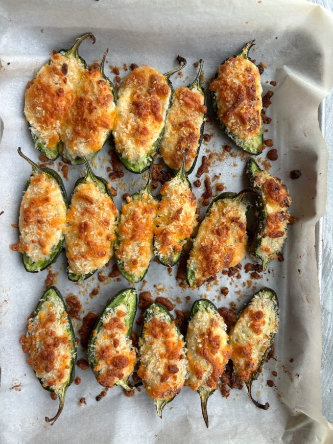 overhead shot of jalapeño halves stuffed with cheese and topped with breadcrumbs on a parchment paper lined sheet tray after being baked