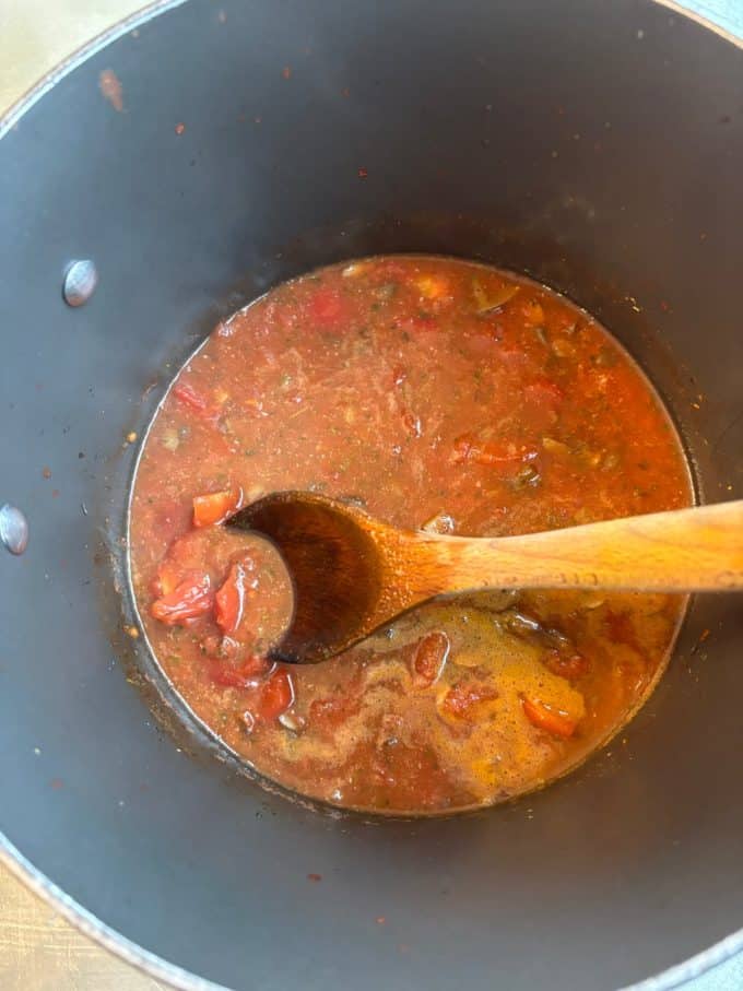 overhead image of nonstick pot cooking chunky tomato soup with a wooden spoon
