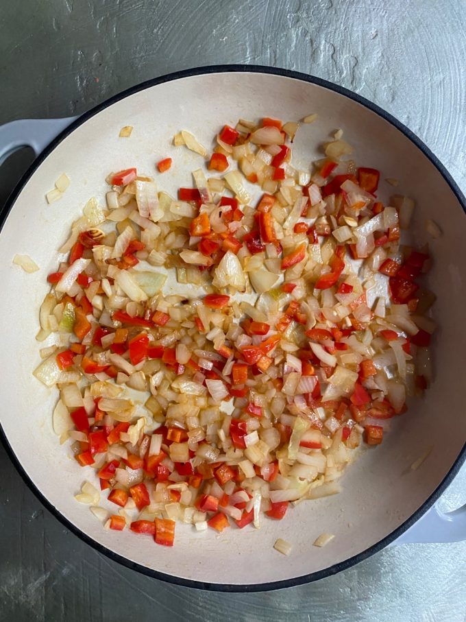 overhead image of a skillet cooking diced red bell peppers, diced onions, and diced garlic