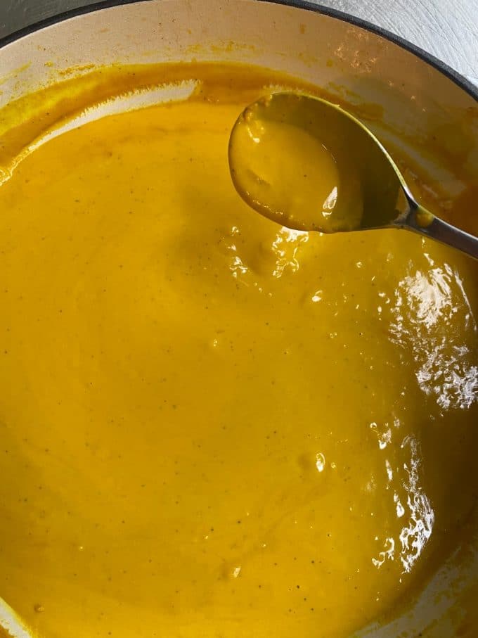 overhead image of a spoon filled with yellow turmeric sauce above a pot filled with the sauce