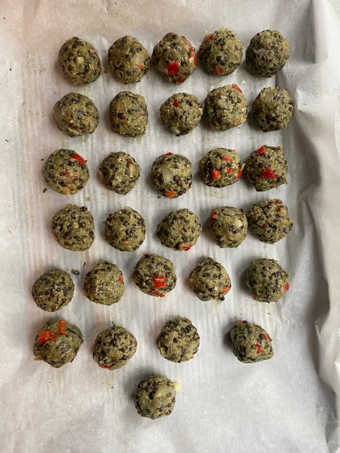an overhead image of a sheet tray lined with parchment paper. On top are 6 rows of 5 lentil meatballs