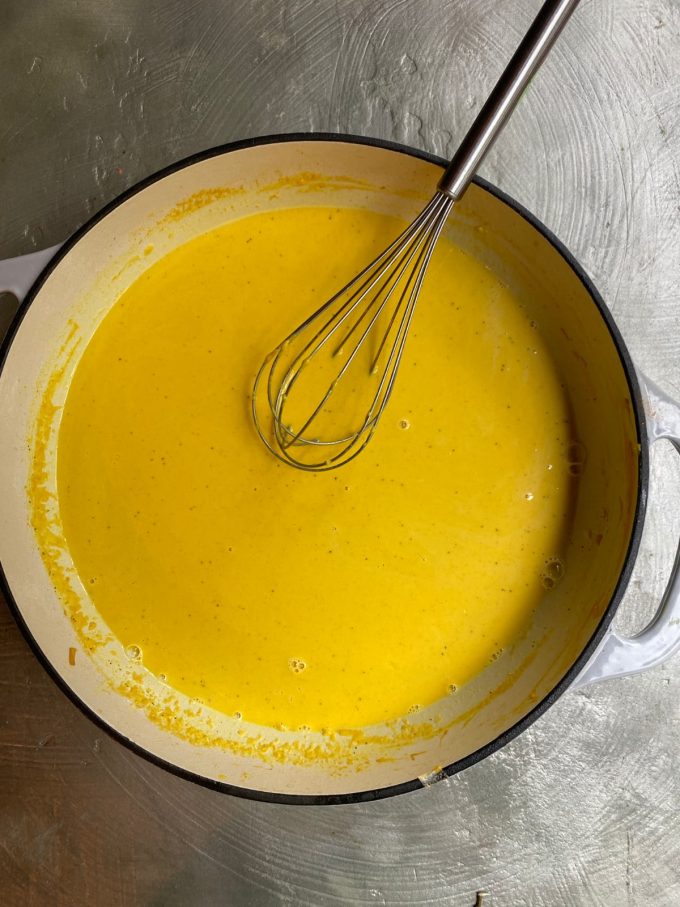 overhead image of a ceramic pot cooking a yellow sauce with a whisk