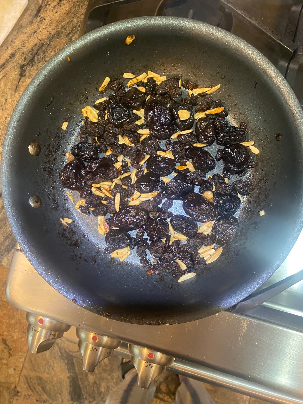 overhead view of a nonstick skillet cooking sliced almonds, raisins, and prunes