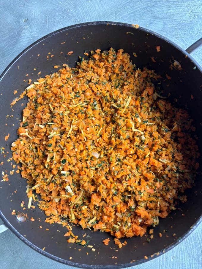 overhead image of a skillet filled with the carrot rice ingredients. It is an orange-hued mixture of shredded carrots, rice, shredded coconut, herbs and spices.
