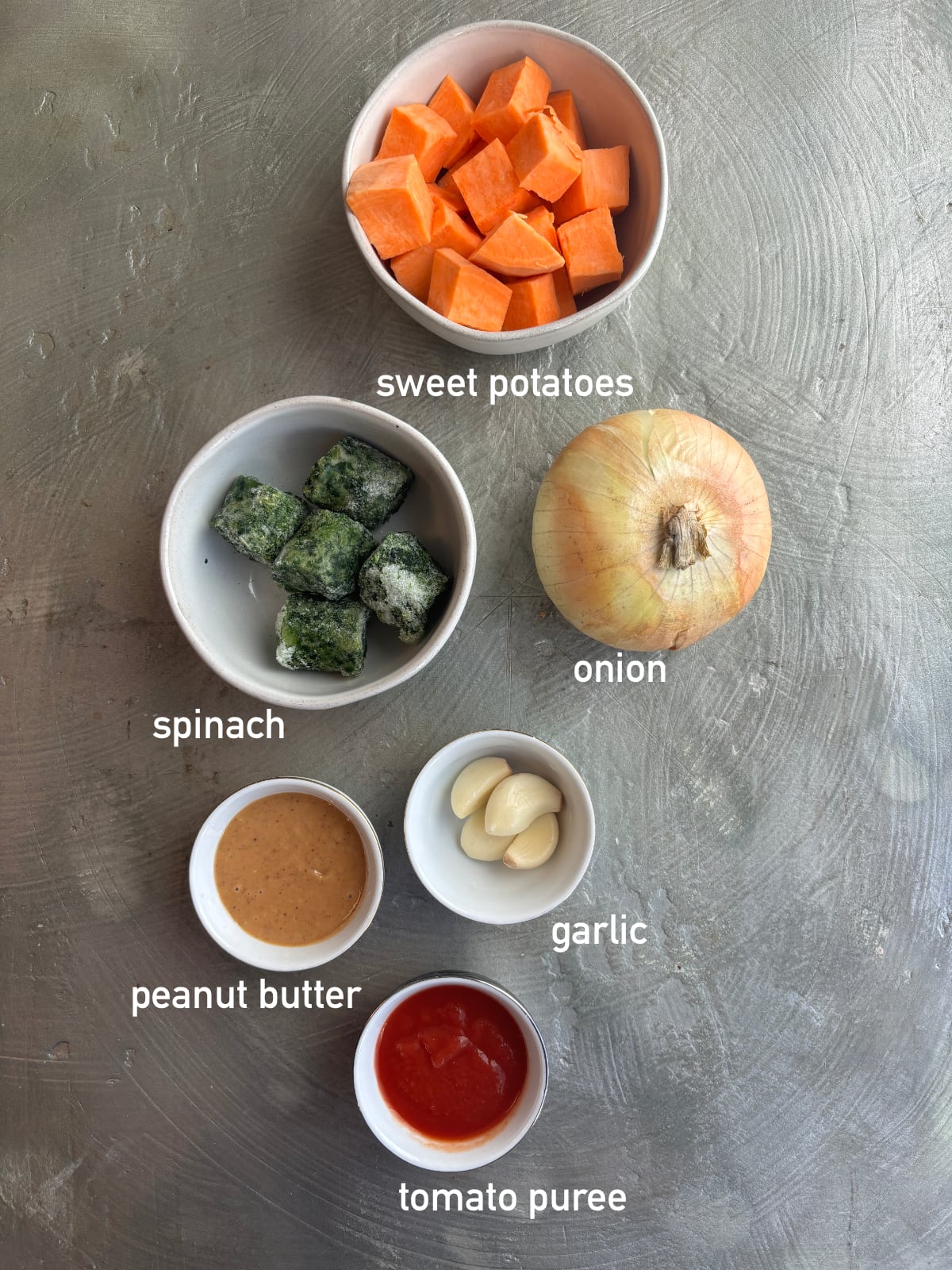 overhead image of the ingredients needed to make peanut soup. Each ingredient is in its own bowl and labeled with white text