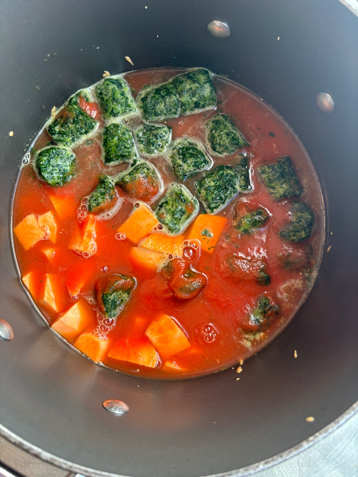 overhead image of a nonstick pot cooking red tomato puree, orange sweet potatoes, and green spinach