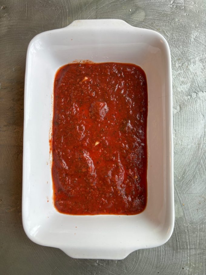 overhead image of a white baking dish with a layer of tomato sauce inside