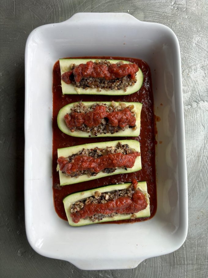 overhead image of zucchini boats filled with quinoa and vegetable filling, topped with tomato sauce
