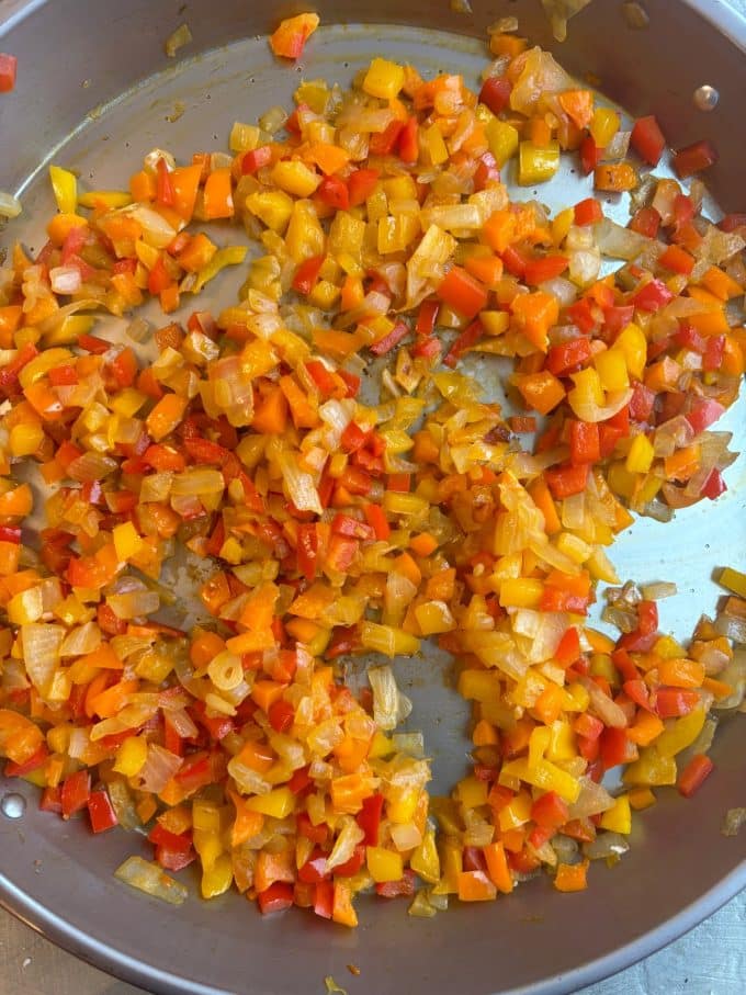 overhead image of a paella pan cooking diced red, orange and yellow bell peppers, and diced onions.