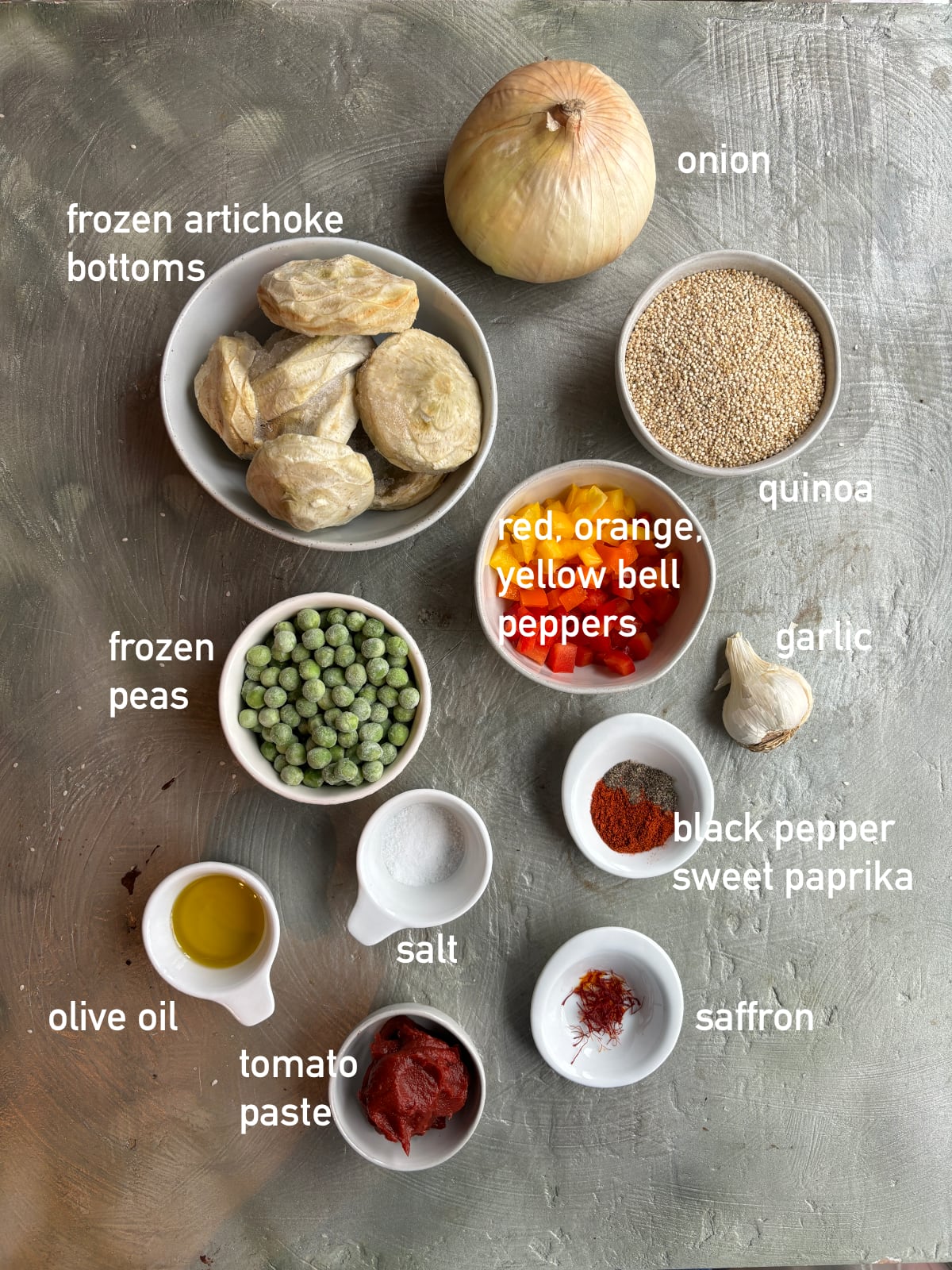 overhead image of the ingredients needed to make quinoa paella. Each ingredient is in a small white bowl and labeled with white text