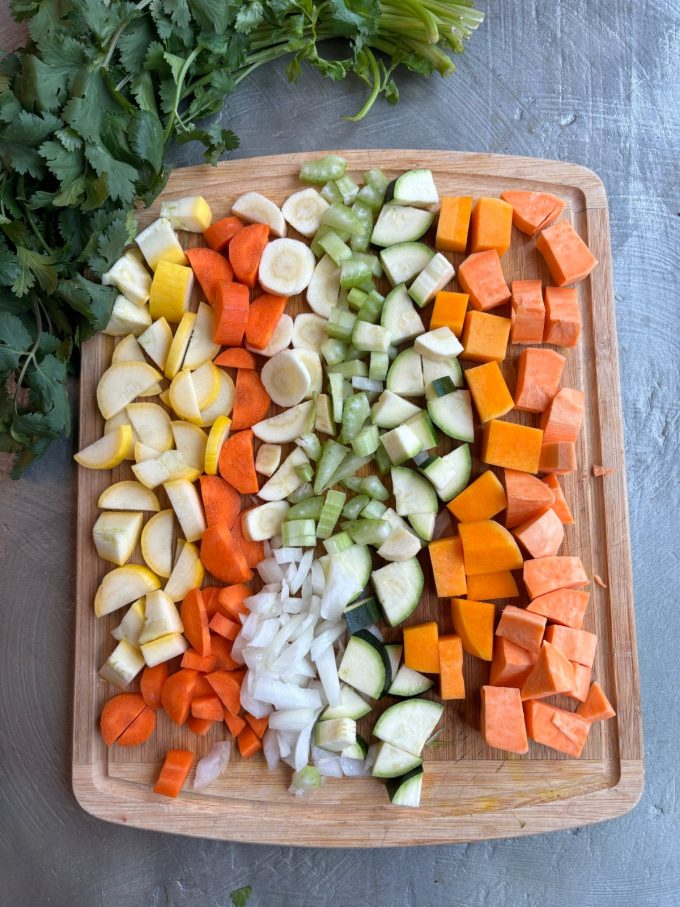 overhead image of a wooden cutting board. Diced vegetables are in rows on top of the cutting board.
