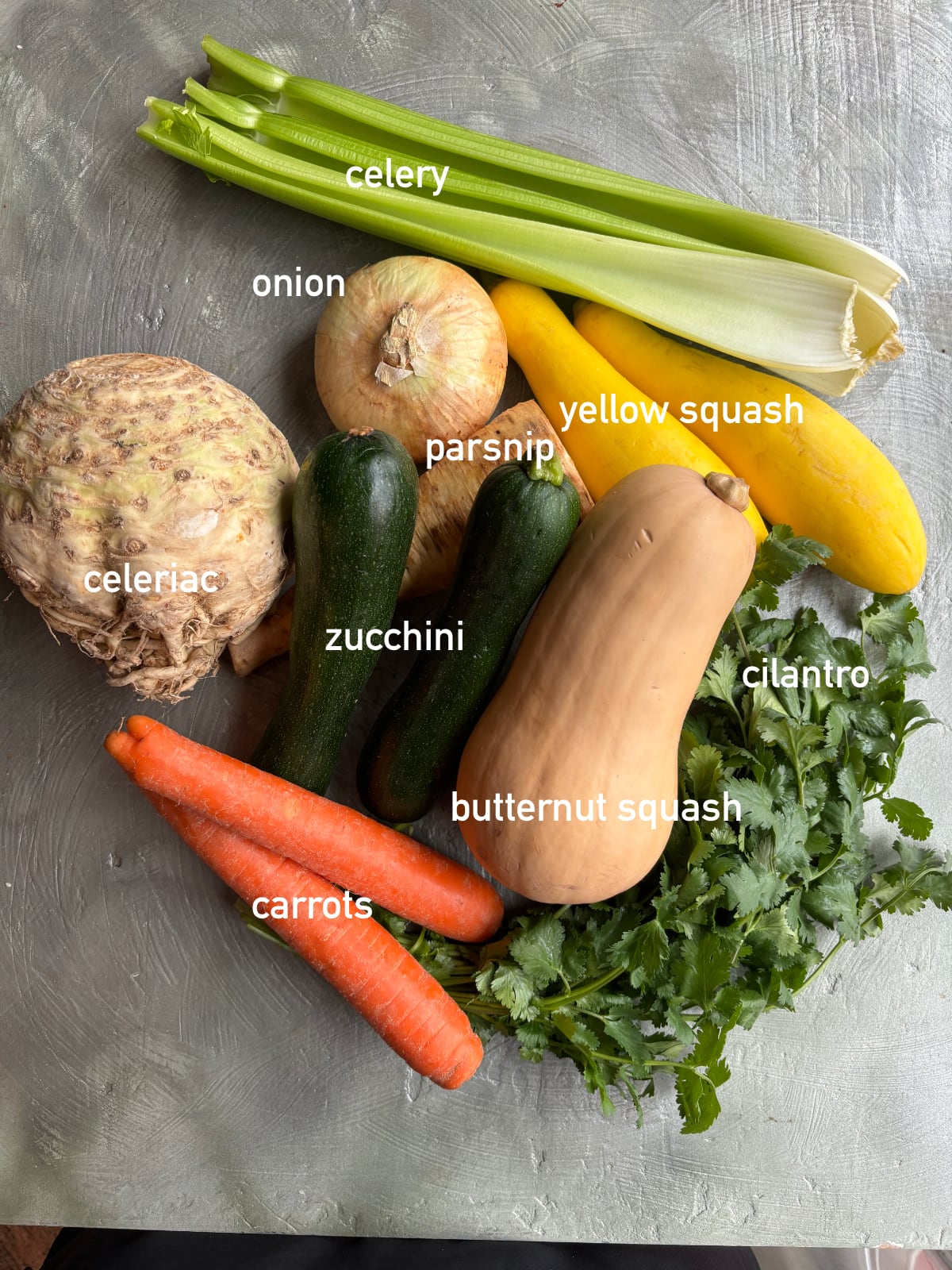 overhead image of the ingredients needed to make vegetable soup. Each ingredient is whole and labeled with white text