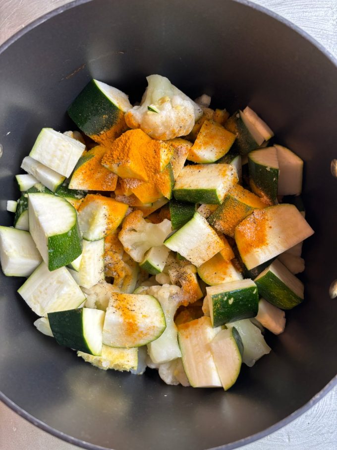 overhead image of chopped zucchini and cauliflower dusted with spices in a nonstick pot