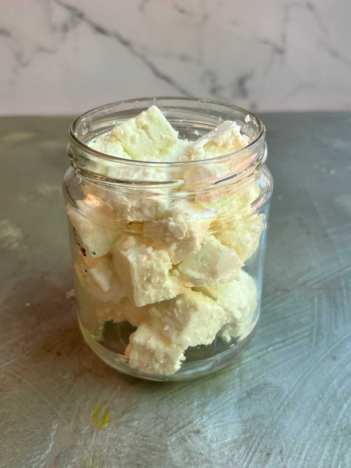 cubes of feta cheese inside a clear glass jar with no lid