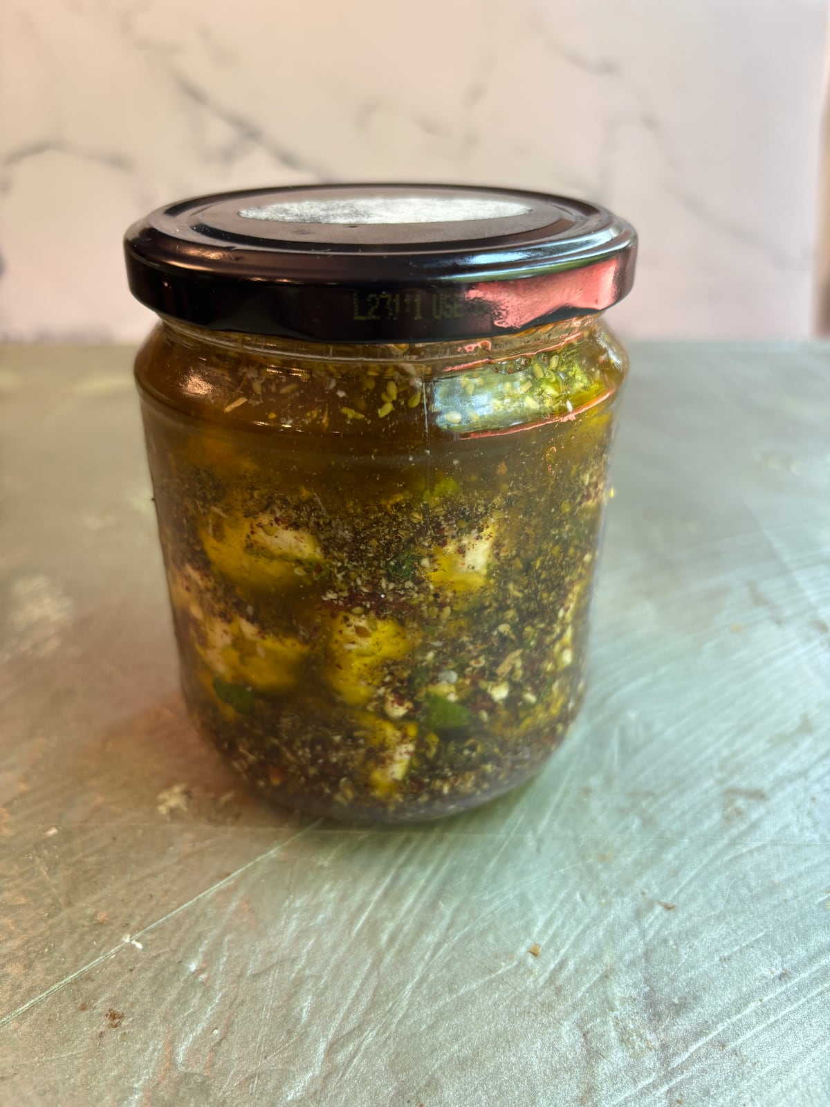 The glass jar containing the cubed feta and marinade with a black lid on top.