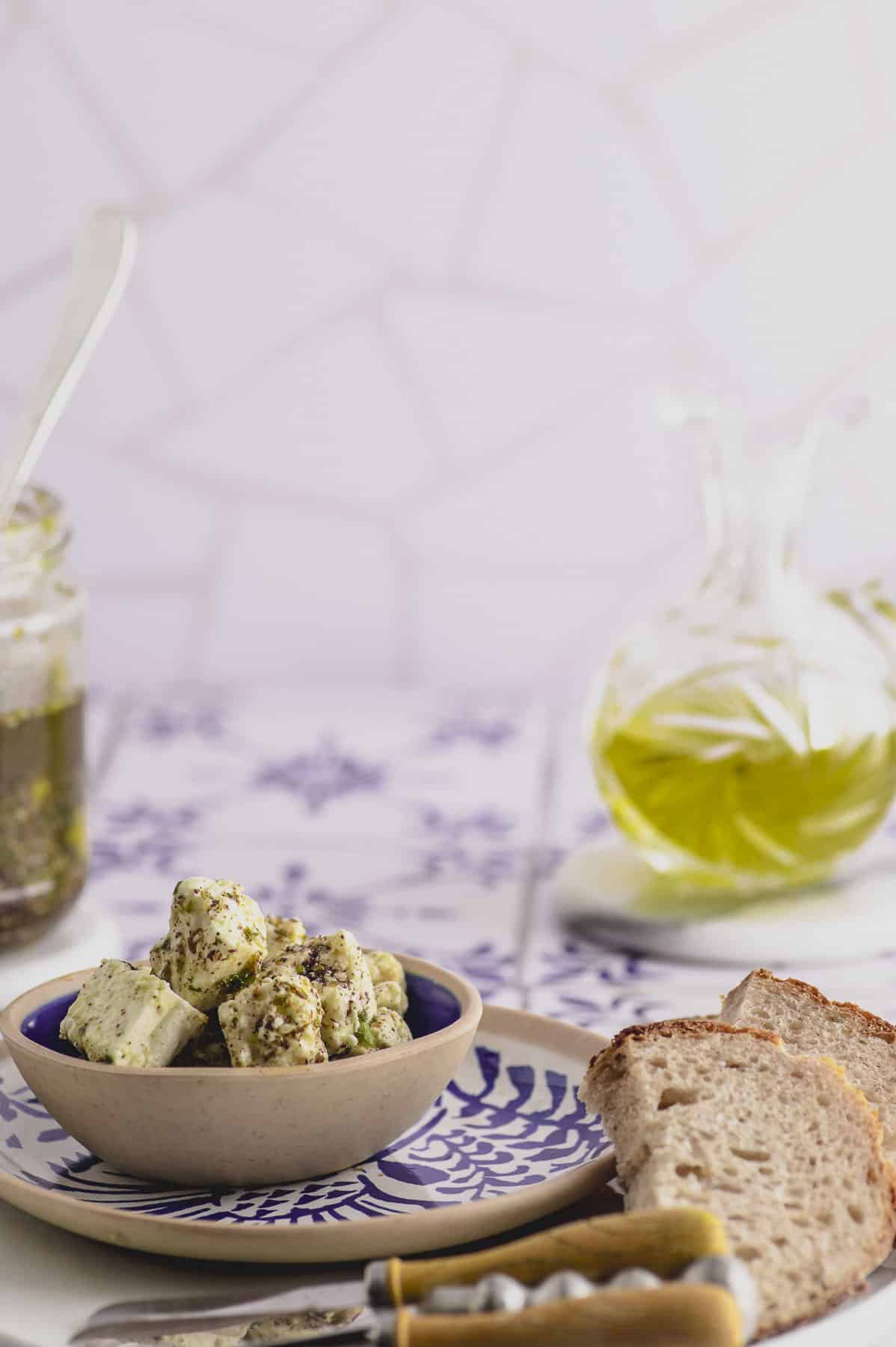 A bowl with marinated feta, a bottle of olive oil and some slices of bread