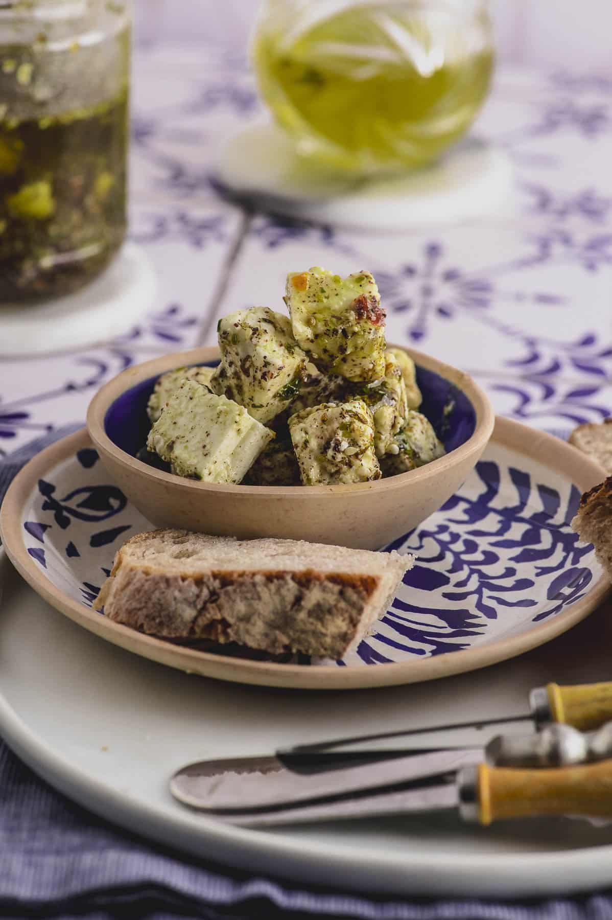 Close up of a small bowl with marinated feta cheese next to a piece of bread