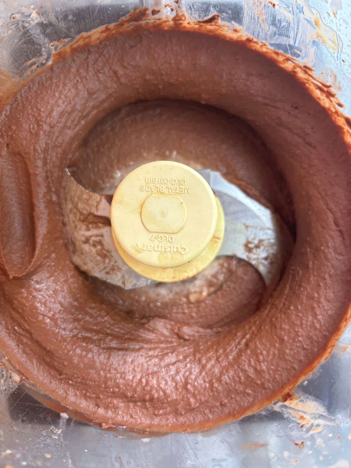 overhead image of a food processor after blending chocolate hummus. It is a smooth chocolate-colored dip.