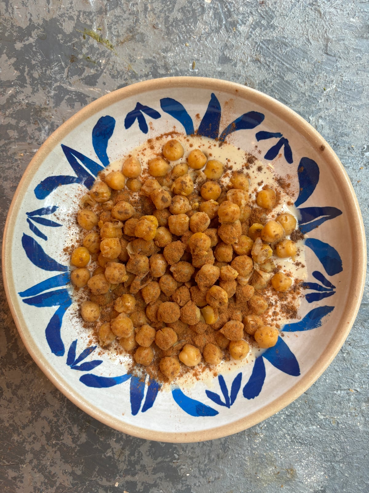 overhead image of a blue and white bowl with tahini inside. The tahini is topped with chickpeas that have been coated with spices.