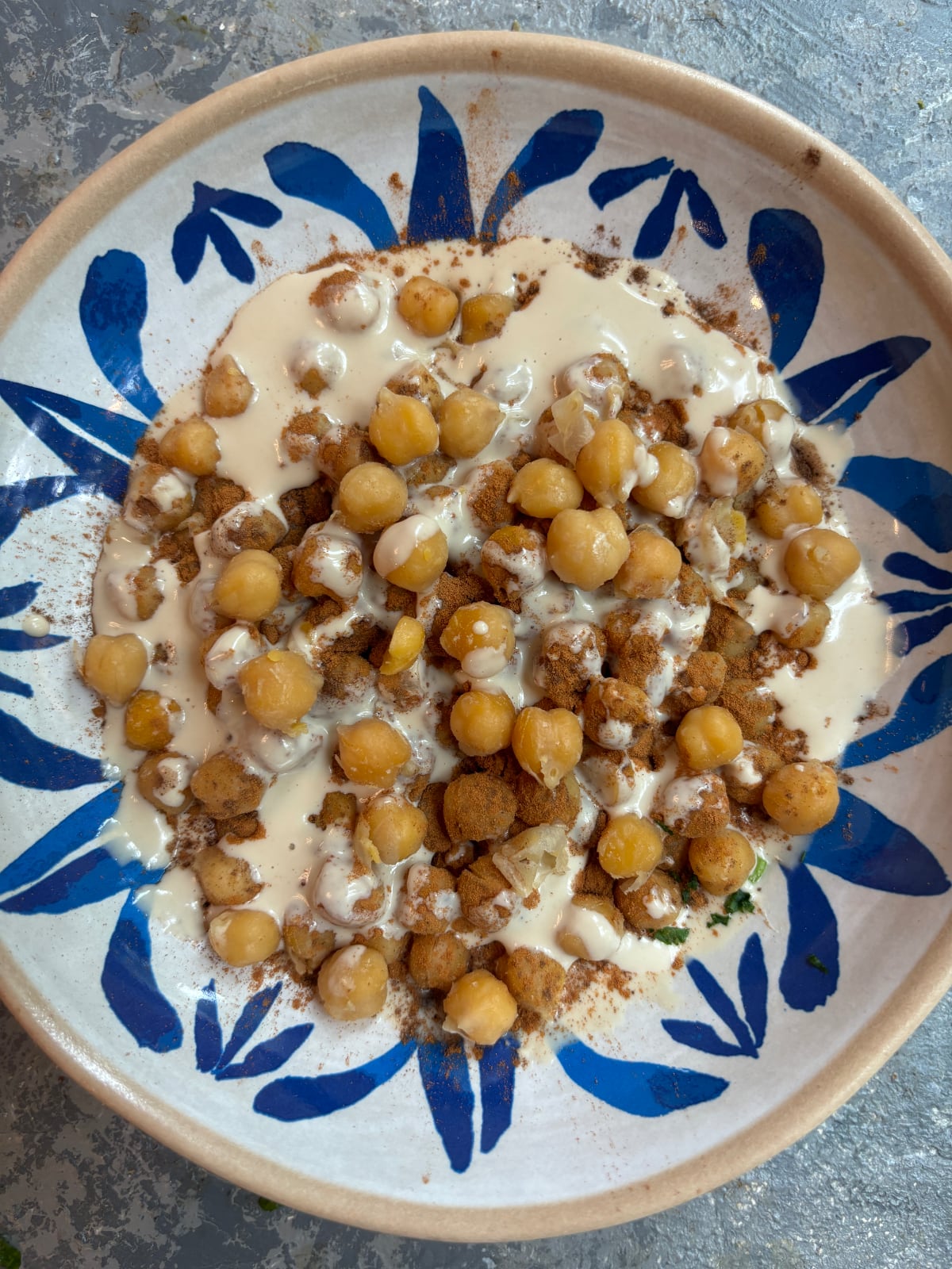 overhead image of a blue and white bowl containing a mixture of tahini, chickpeas, and spices.