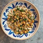 overhead image of a blue and white bowl filled with Musabaha. The ingredients are tahini, chickpeas, pine nuts, spices, and chopped fresh parsley.