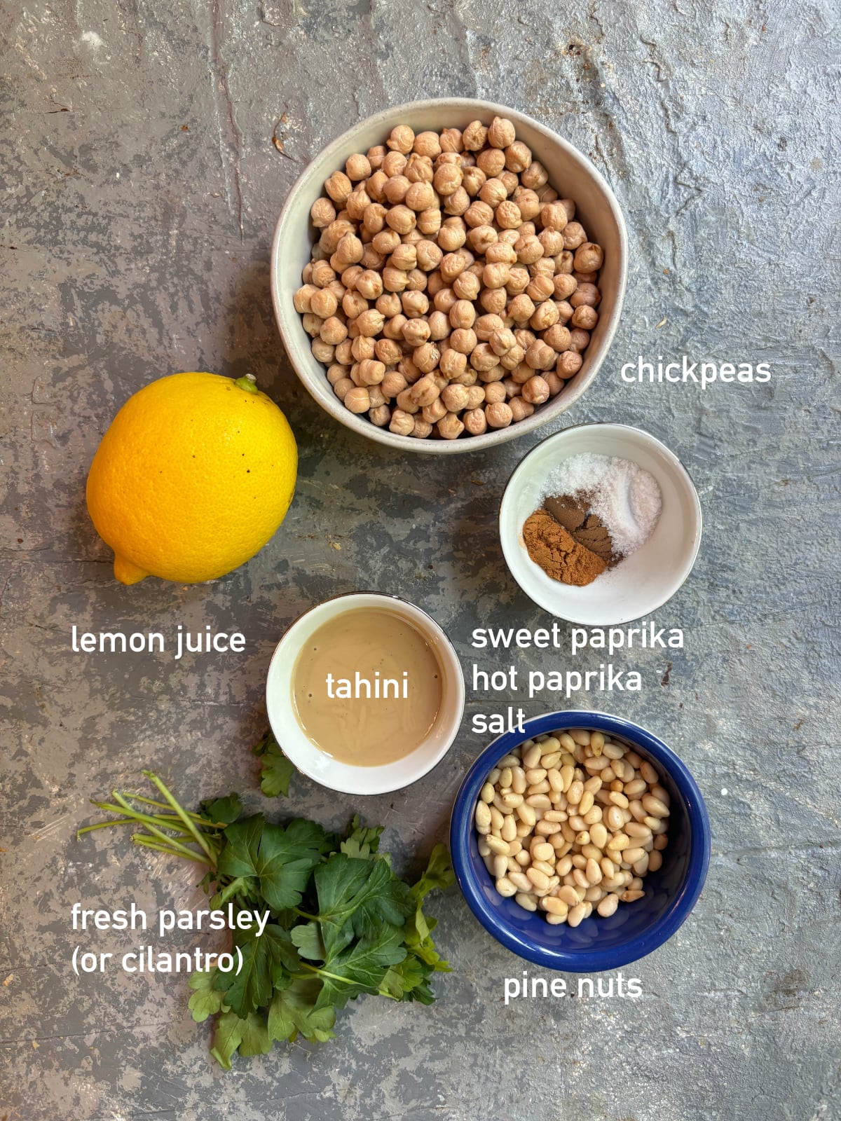 overhead image of the ingredients needed to make Musabaha. Each ingredient is in it's own small bowl and labeled with white text.