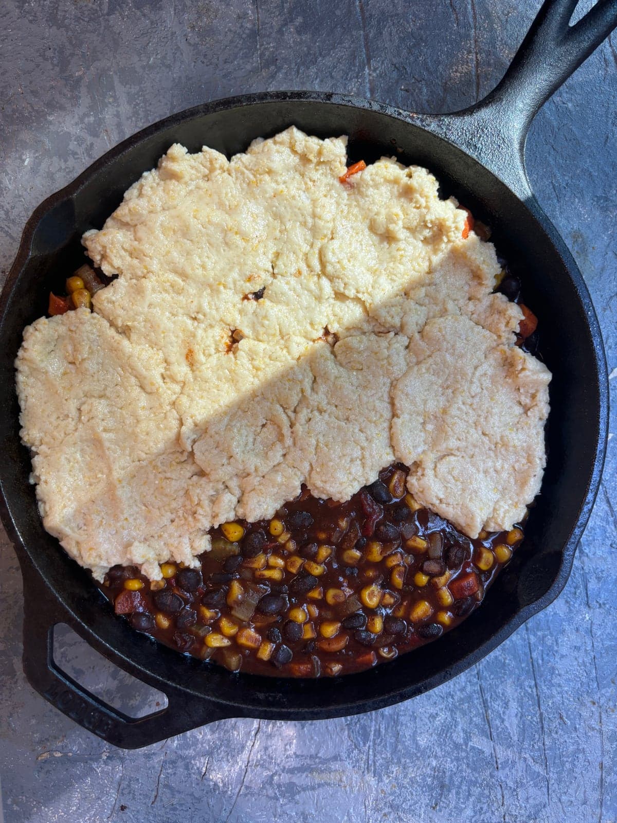 overhead image of a cast iron skillet filled with black bean chili and partially topped with cornbread batter