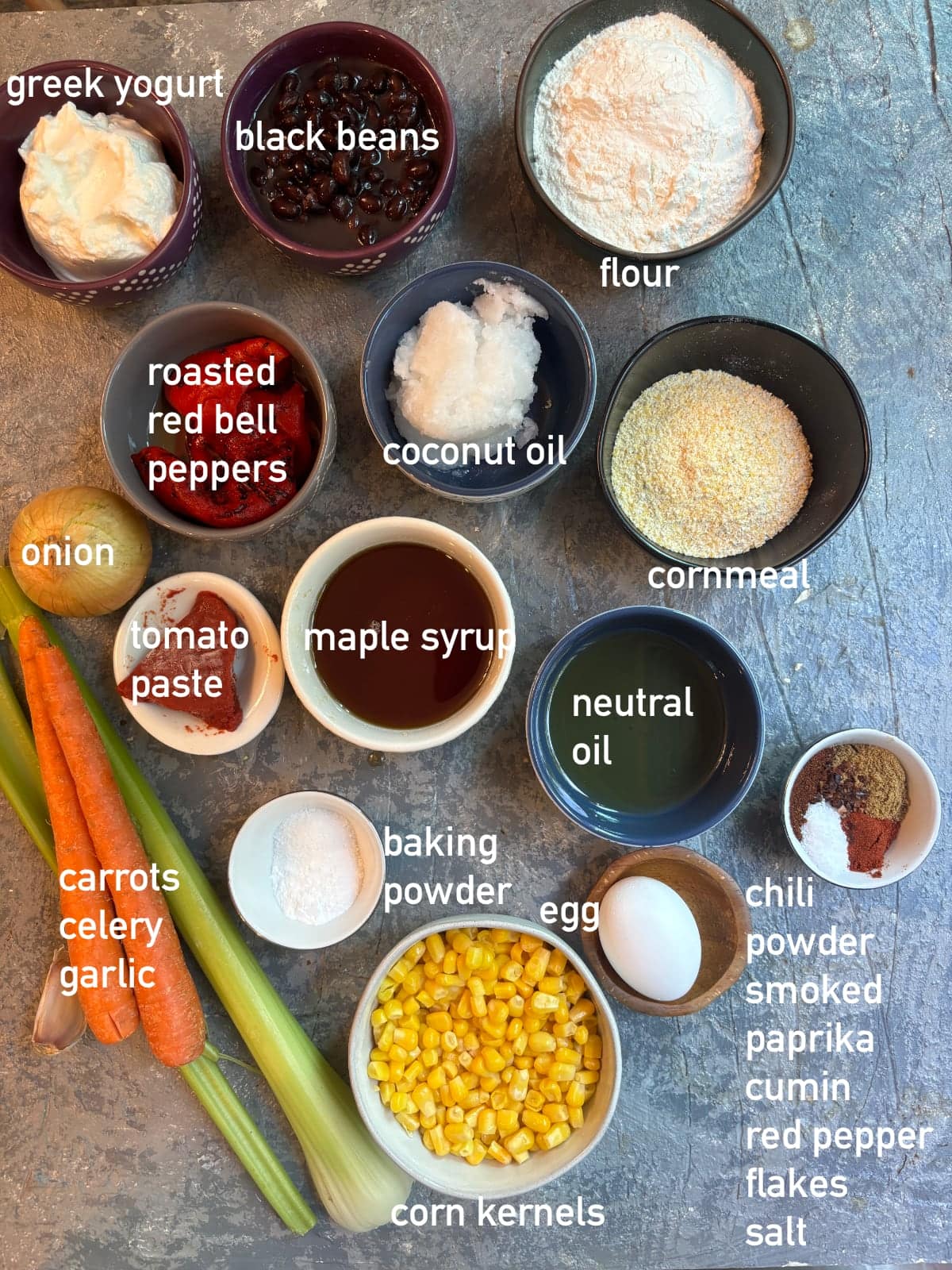overhead image of the ingredients needed to make Chili Cornbread Casserole. Each ingredient is in it's own bowl and labeled with white text