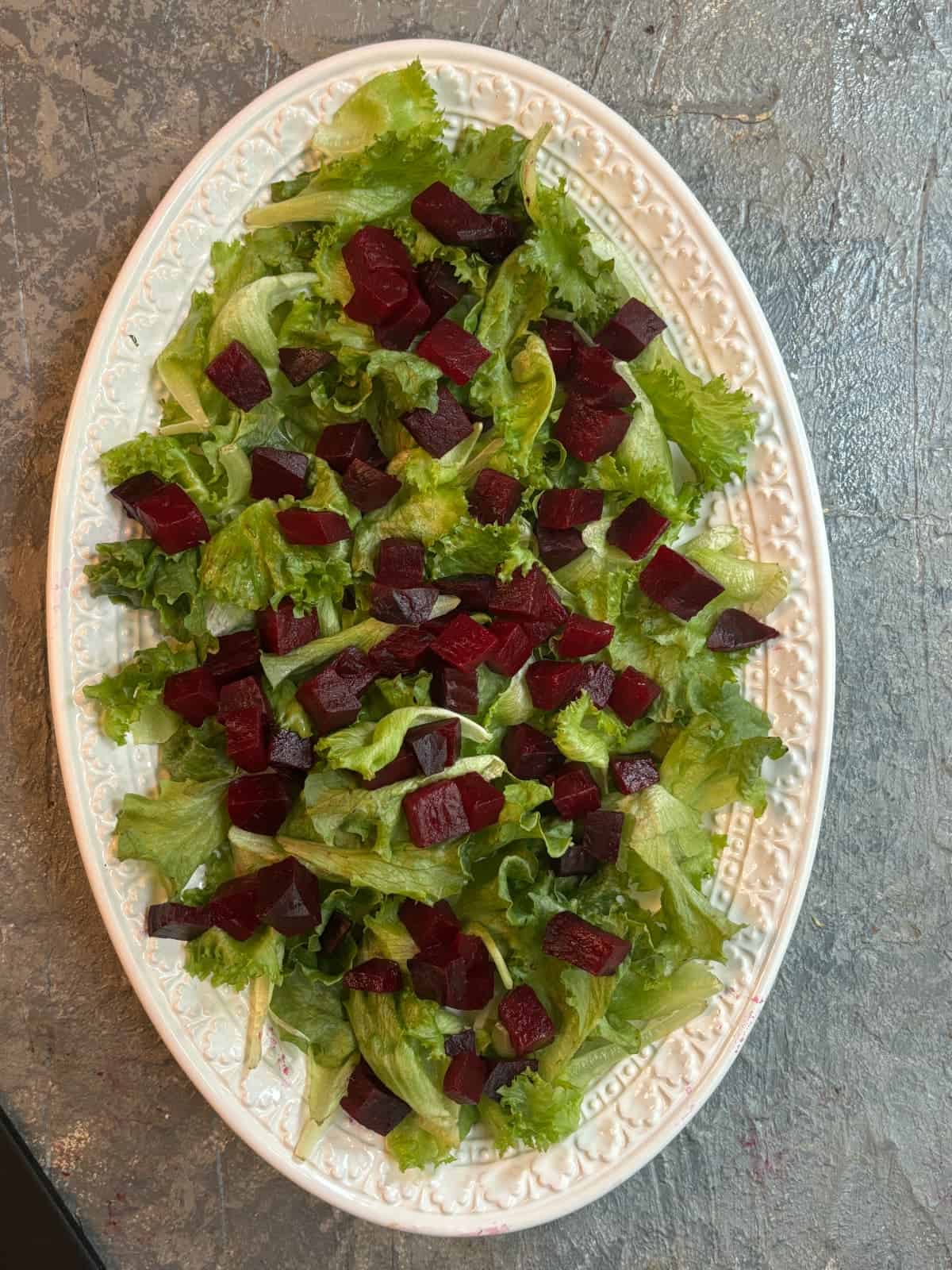 overhead image of a white oval platter topped with salad greens and diced cooked red beets
