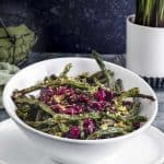 an asymmetrical white bowl on top of a white plate. The bowl is filled with roasted green beans and cranberries.