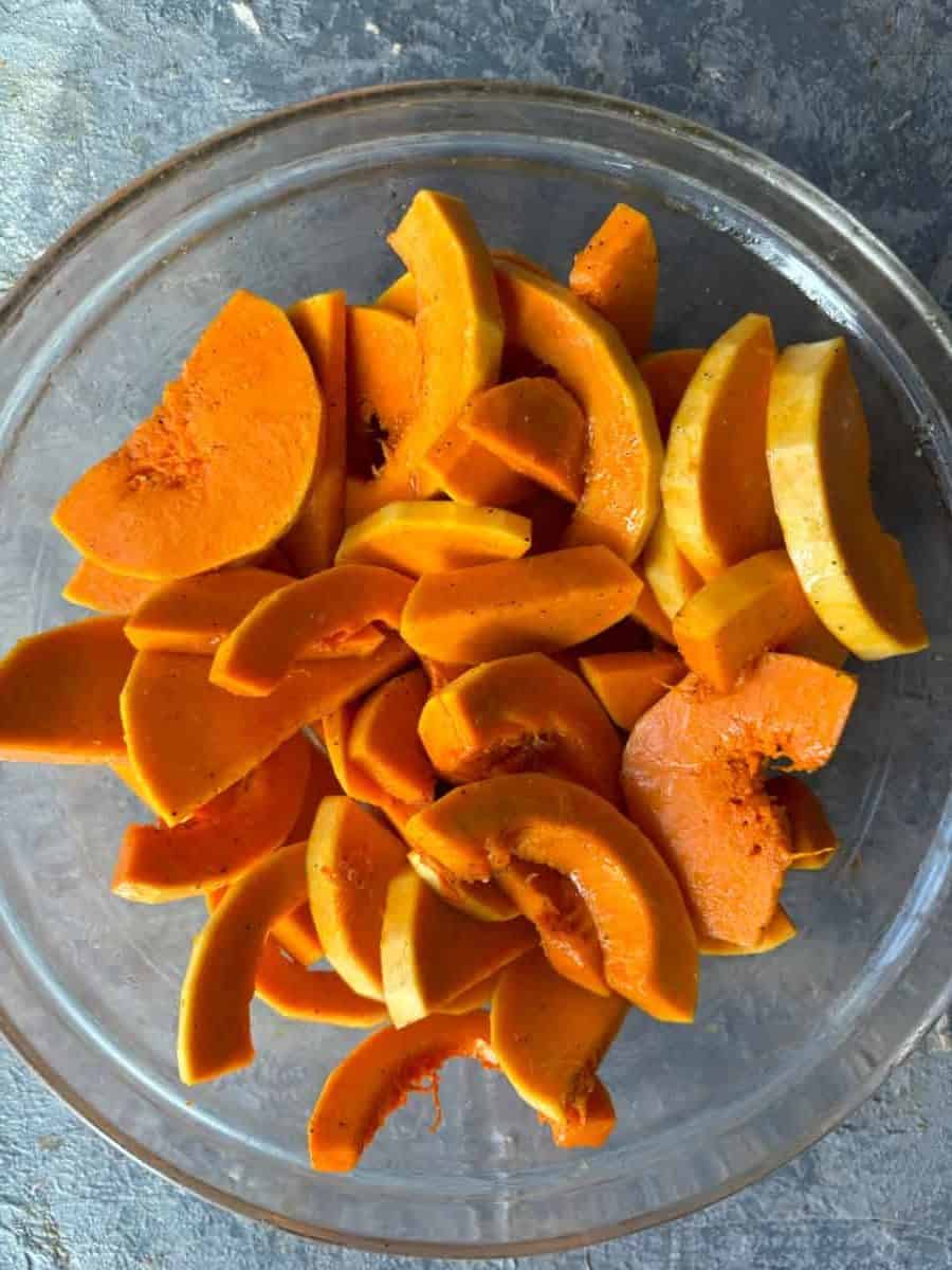 overhead image of a clear glass mixing bowl with slices of raw orange honeynut squash inside