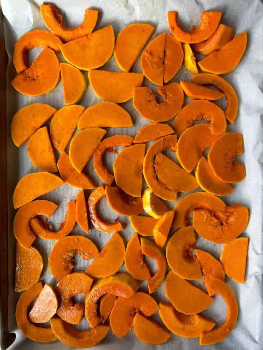 overhead image of orange slices of raw honeynut squash arranged closely together on top of parchment paper.