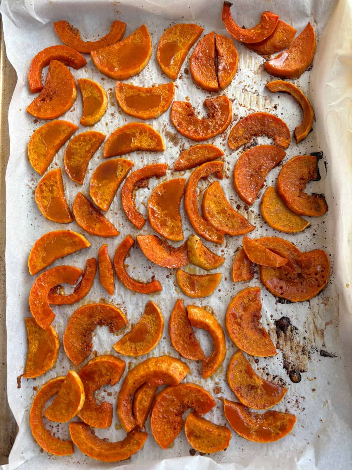overhead image of orange slices of honeynut squash after being cooked on parchment paper.