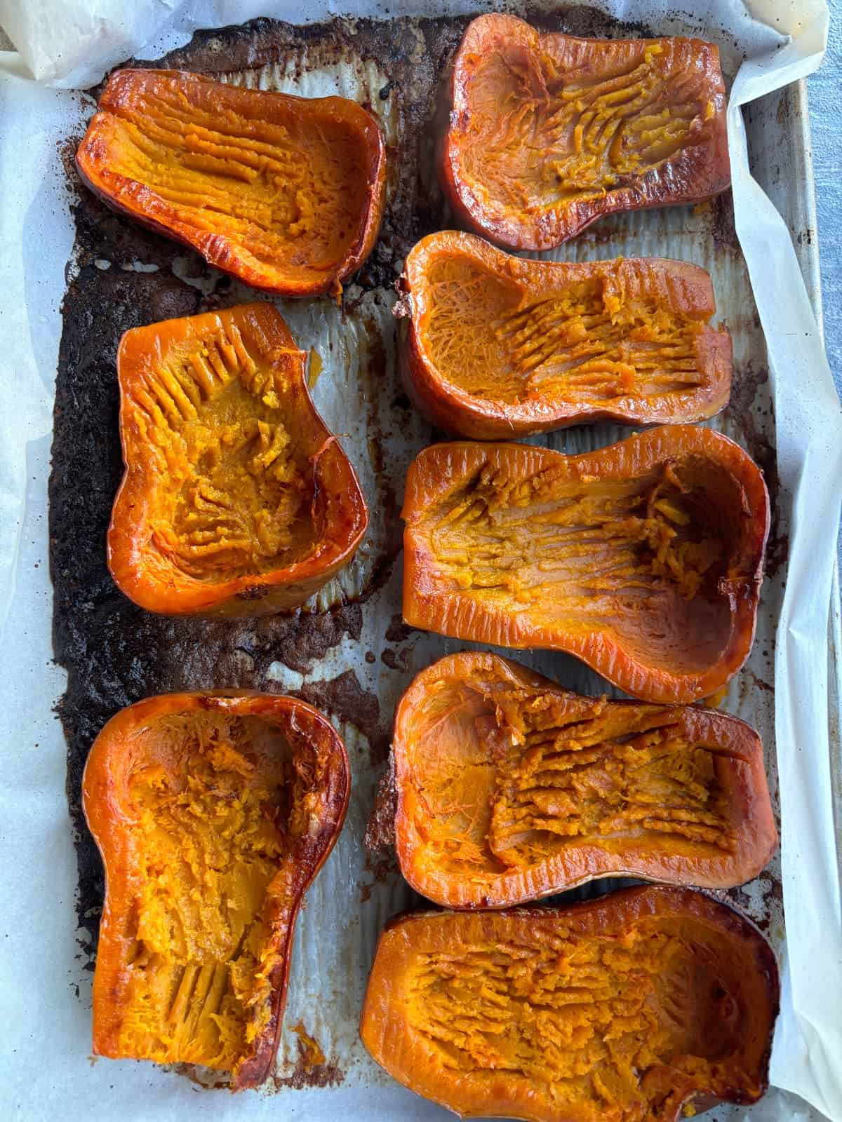 overhead image of 8 halved and roasted honeynut squash, cut side up. The flesh has been scooped out with a fork so some of the flesh is left inside the skins.