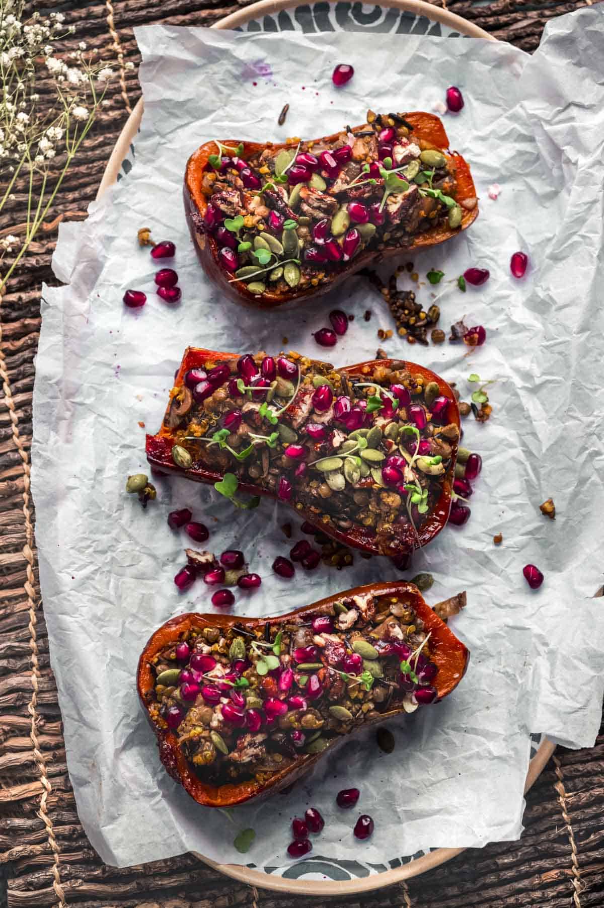 overhead image of 3 honeynut squash halves stuffed with a wild rice mixture and topped with pomegranate seeds, nuts, and micro greens.