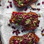 overhead image of 3 honeynut squash halves stuffed with a wild rice mixture and topped with pomegranate seeds, nuts, and micro greens.
