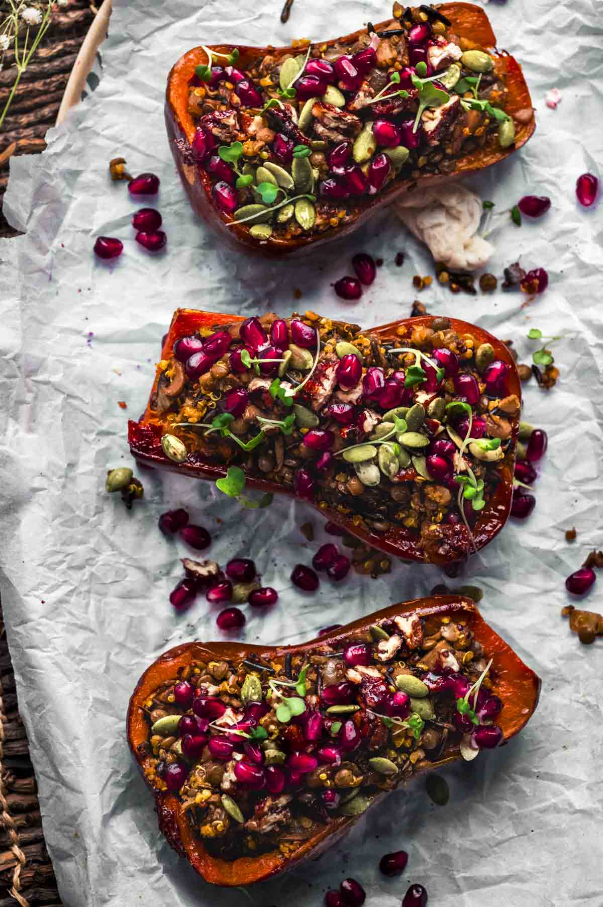 overhead image of 3 honeynut squash halves stuffed with a wild rice mixture and topped with pomegranate seeds, nuts, and micro greens.