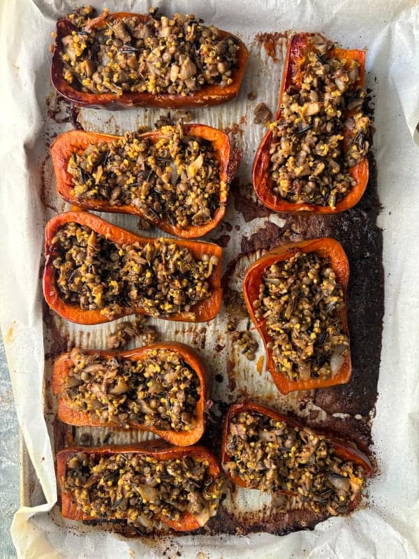 overhead image of 8 halved honeynut squash that have been roasted and stuffed with a mushroom, onion, rice mixture.