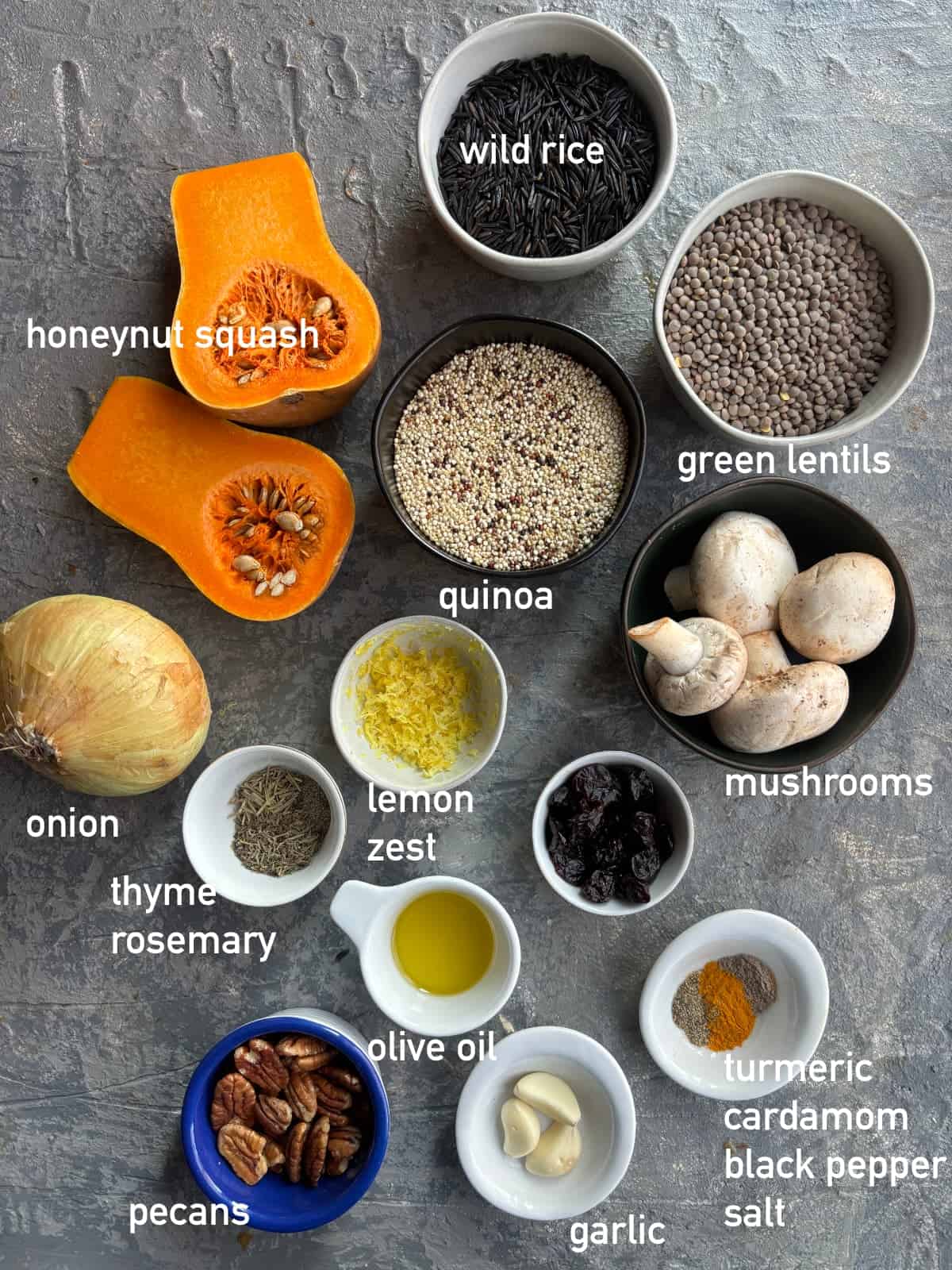 overhead image of the ingredients needed to make stuffed honeynut squash. Each ingredient is in it's own small bowl and labeled with white text.