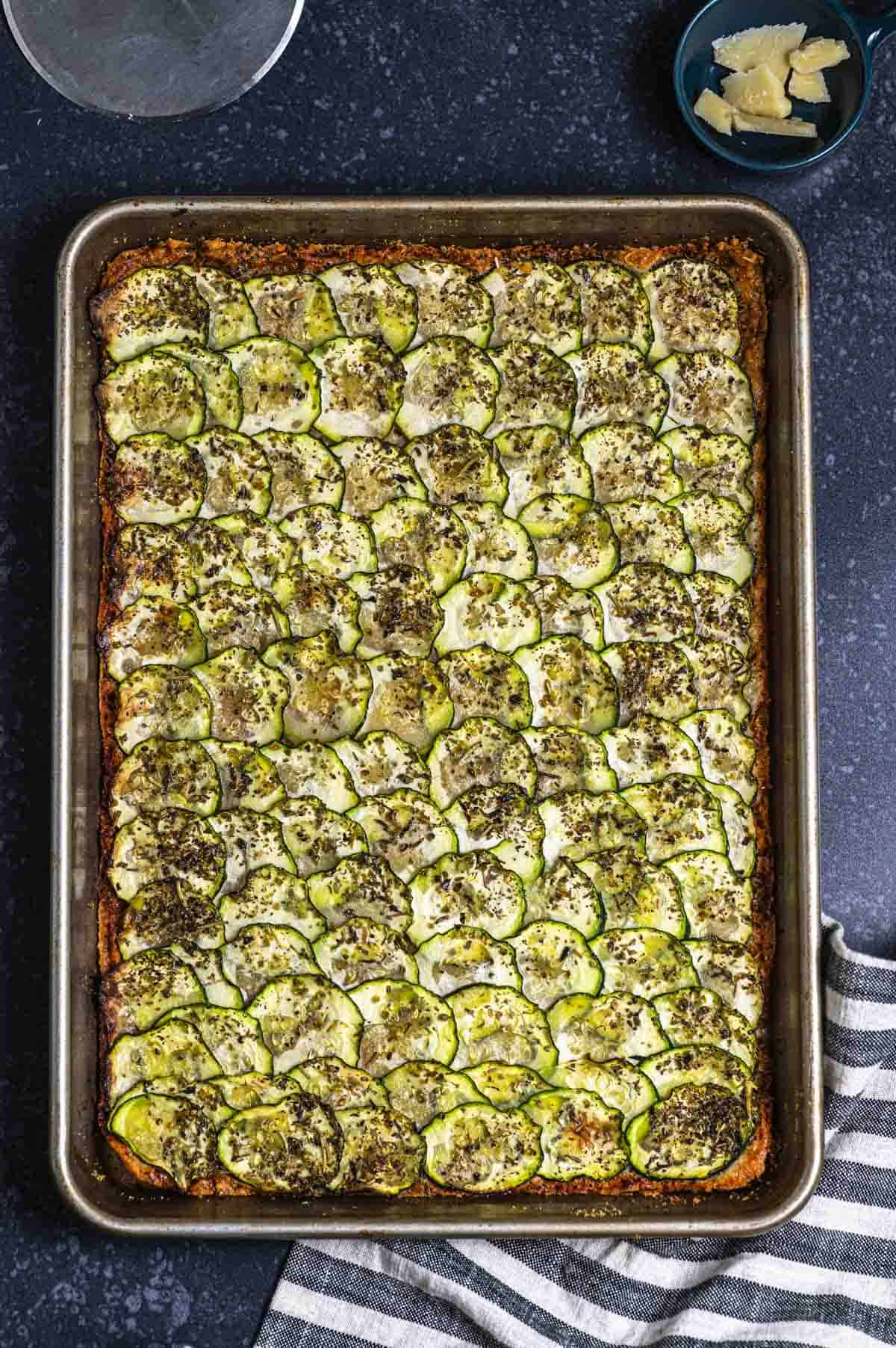 Overhead view of a baking sheet with baked parmesan topped with thinly sliced zucchini